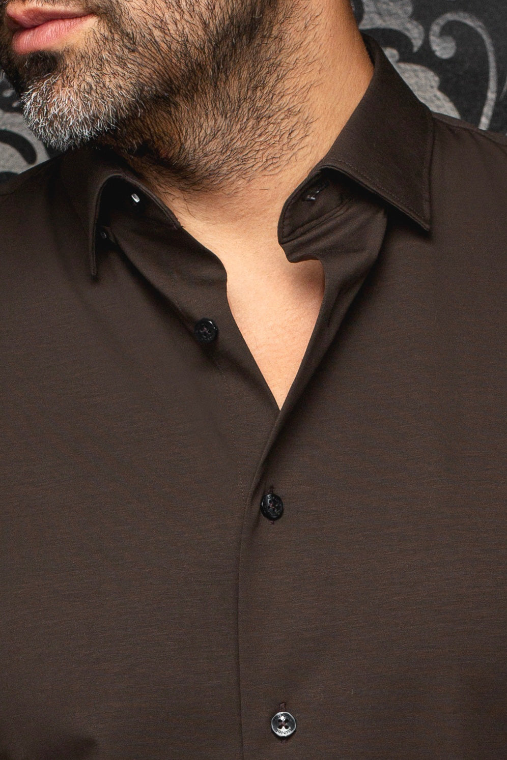 Col ouvert d’une chemise brune foncé, avec patte et boutons noirs pour homme par Au Noir, en gros plan