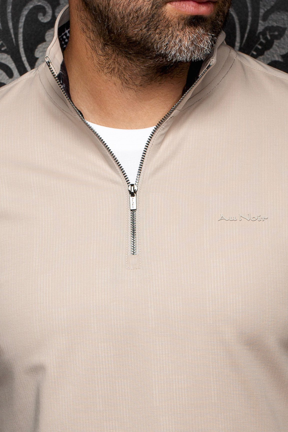Gros plan de la veste sport beige à demi-glissière, dents foncées, logo ton sur ton et tissu texturé pour homme par Au Noir