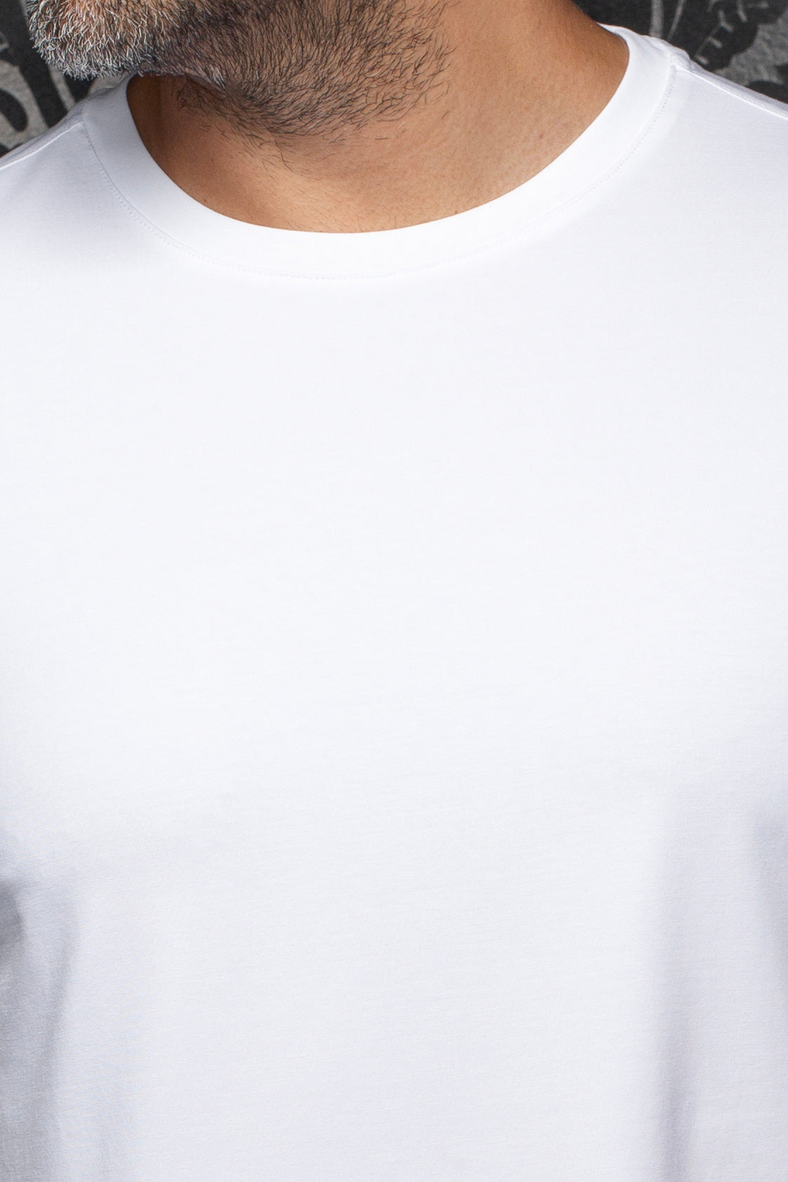Détail du col rond d’un T-Shirt blanc uni, montrant l’encolure cousue et le jersey lisse pour homme par Au Noir