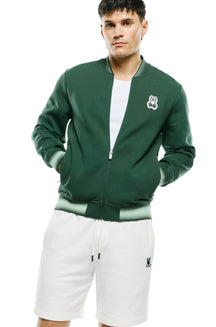 Front model view of men's dark green zip bomber jacket with bunny chest patch and striped rib trims by Psycho Bunny