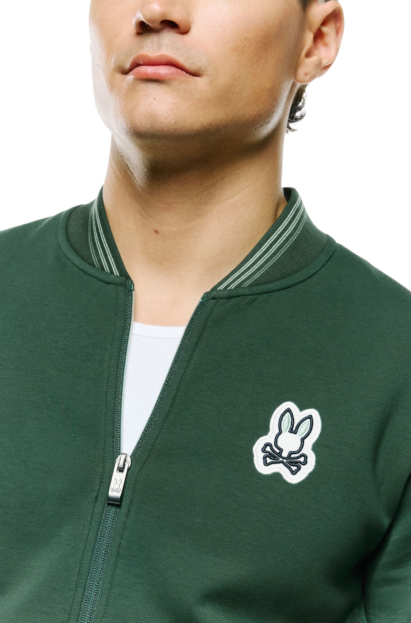 Psycho Bunny men's dark green bomber jacket collar, bunny skull chest patch and zipper pull, close-up